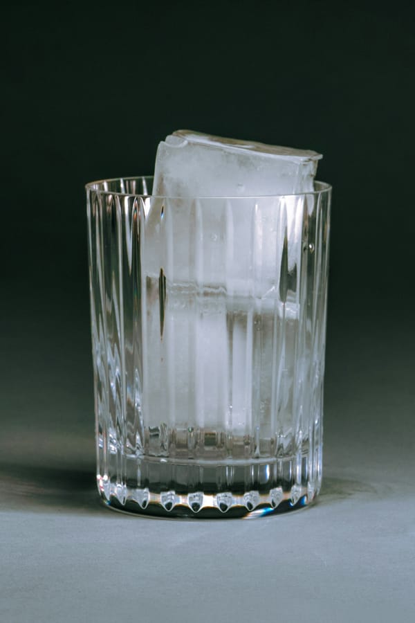 Photograph of a glass full of ice cubes against a stark gray background