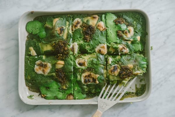 A white casserole dish on a marble surface, containing green lasagna made with tofu