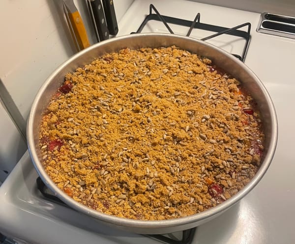 A berry crisp in a metal pan topped with sunflower seeds and streusel